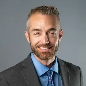 tm6-300x300 Smiling man in suit with blue shirt.